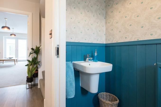 łazienka z niebieską boazerią i tapetą z pawim piórem