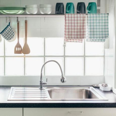 Interno della cucina di casa. Utensili da cucina su un sistema di ringhiere e mensola con piatti sopra una finestra.; ID Shutterstock 698380921