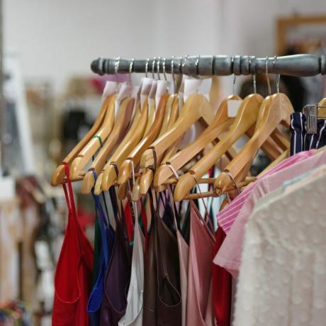 Et stort sortiment af farverigt tøj til kvinder på en butiksbaggrund. Forskellige fashionable farve skjorter og kjoler i en dyr boutique. Luksus og stilfuld beklædningsgenstand på bøjler. Mode koncept.