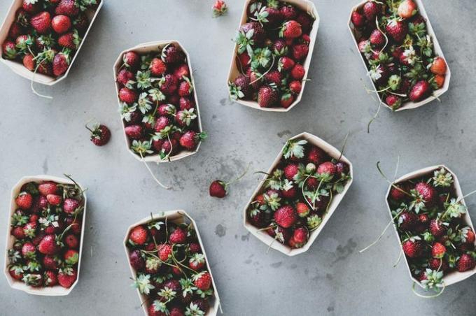 Färsk säsongsbetonad sommarmarknad med frukt. Plattläggning av trädgårdsskörd jordgubbar i miljövänliga plastfria lådor över grå betongbakgrund, ovanifrån