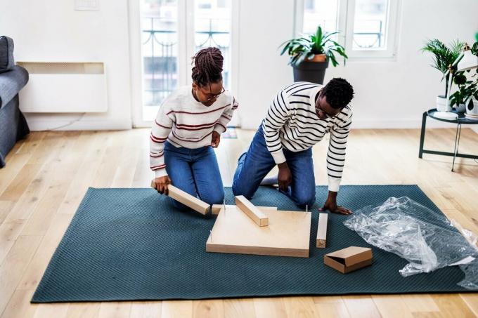 Jauna afrikiečių pora džiaugiasi naujuose namuose montuodama medinį stalą.