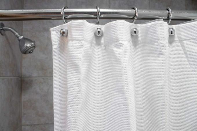 una cortina de ducha blanca en una ducha vacía con agua en plano medio