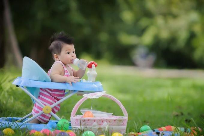 Lindo bebé bebiendo leche de un biberón en un andador, feliz y se relaja en el jardín, parte importante de la familia.