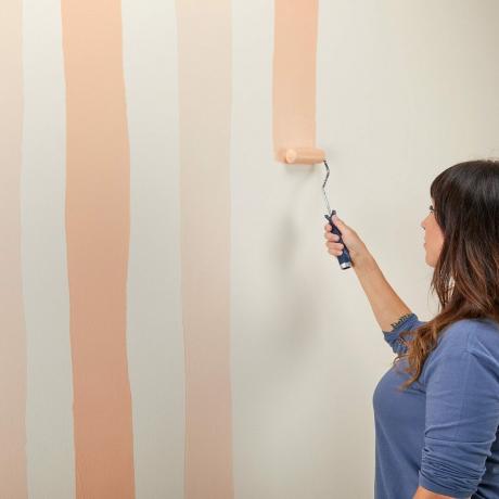 Lady dipinge il muro con il rullo di vernice
