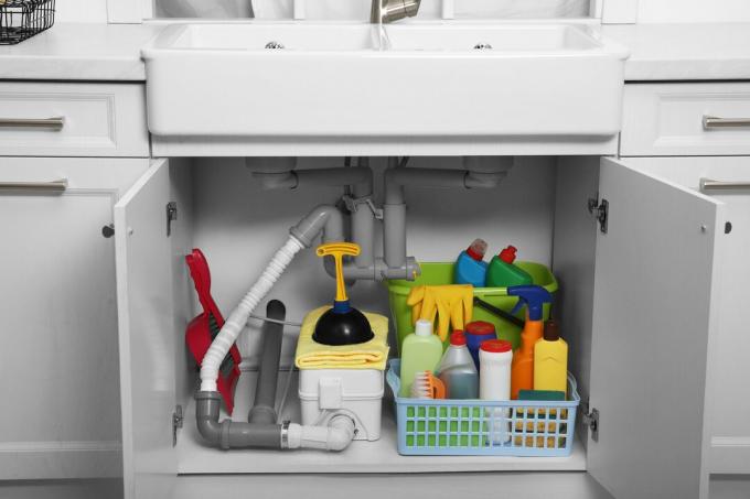 Отворен шкаф под мивката с различни почистващи препарати в кухнята