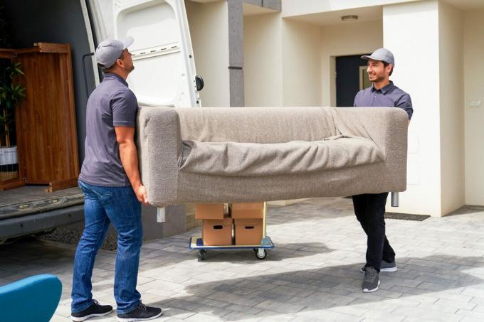 Pristatymo bendradarbiai vyrai iškrauna sofą iš kraustančio furgono šalia namo