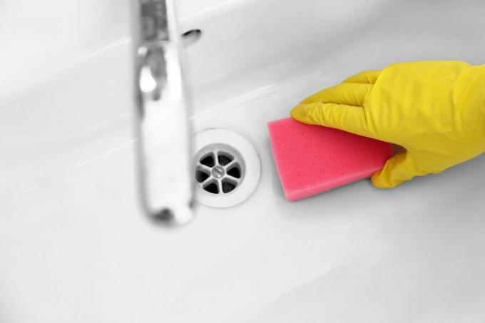 Vrouwelijke hand met spons die een gootsteen in de badkamer schoonmaakt