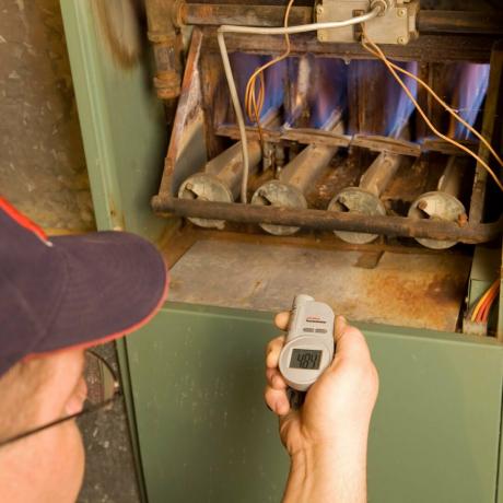 Reparatør med digitalt infrarødt termometer sjekker gassovnens utgangstemperatur