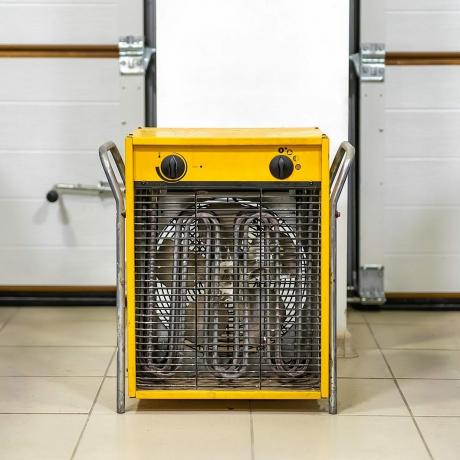 Duży ciężki przemysłowy elektryczny termowentylator w garażu na dwa samochody. Dwa pojazdy zaparkowane do przechowywania w zimie w suchym, ciepłym parkingu na mroźną zimę
