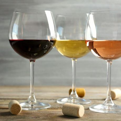 Vyno taurės iš eilės ir kamšteliai ant medinio stalo pilkame fone
