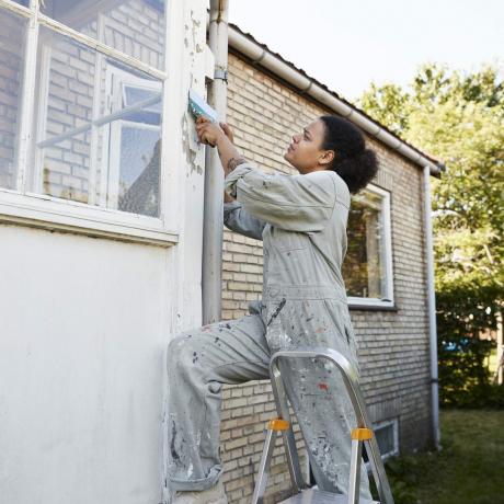 Vrouw schraapt muur van huis tijdens renovatie