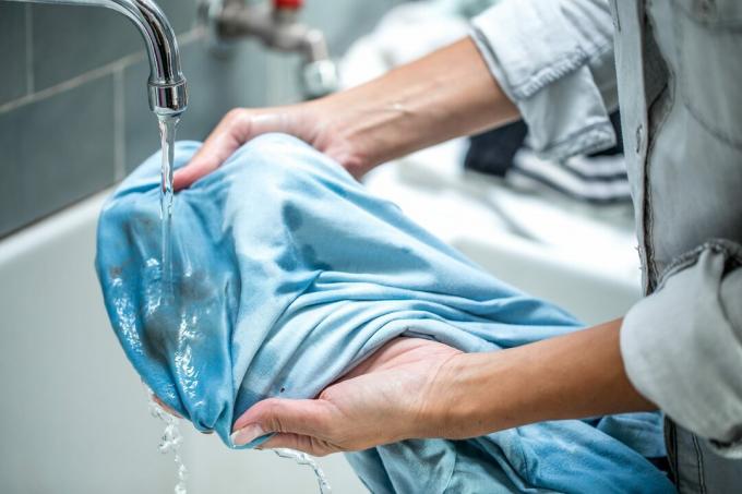 Ženska čisti umazano srajco v kopalniškem umivalniku