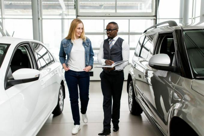 Gerente de ventas muestra a la mujer autos nuevos en la sala de exposición