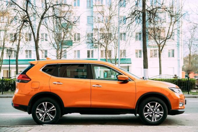 Narančasti automobil Nissan X-Trail treće generacije parkiran na ulici. Pogled sa strane
