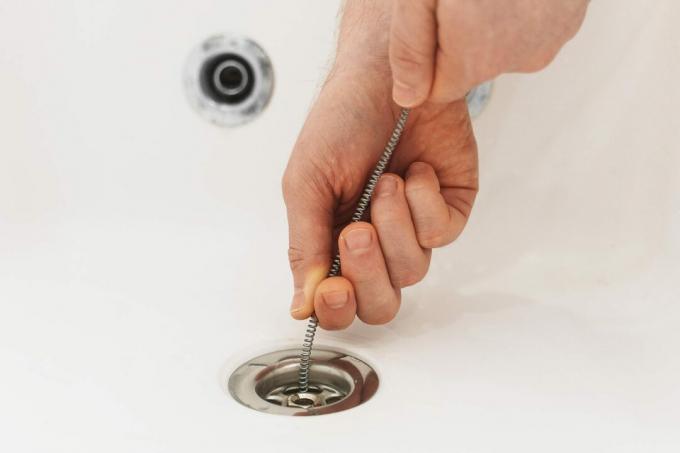 Plombier utilisant un serpent de vidange pour déboucher la baignoire.