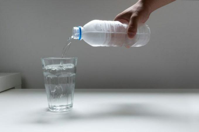 Bildbild hälla plastflaska vatten i glasglas