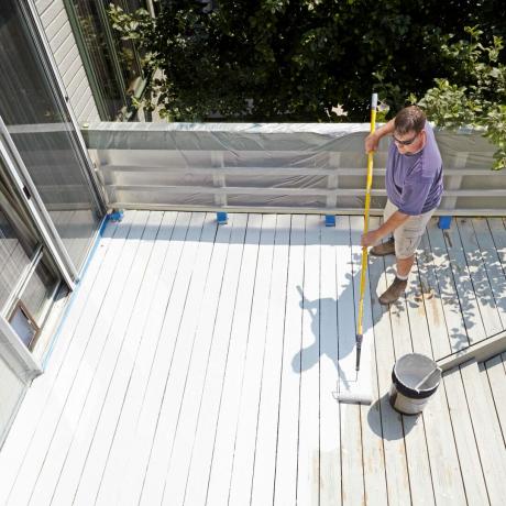 hombre restaurando terraza de madera con pintura blanca