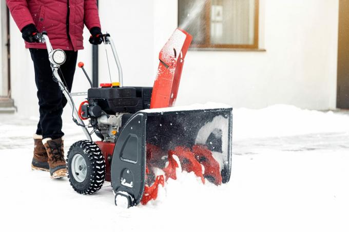 Човек који користи црвену машину за чишћење снега на отвореном. Уклањање снега у близини куће из дворишта