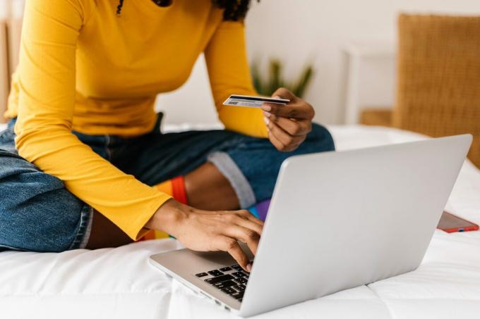 लैपटॉप पर ऑनलाइन खरीदारी करने के लिए क्रेडिट कार्ड का उपयोग करने वाली महिला के हाथों को बंद करें