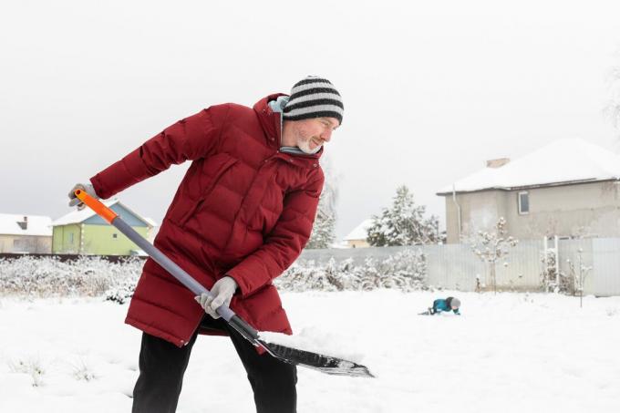 50-летний белый мужчина убирает снег с территории возле своего дома.