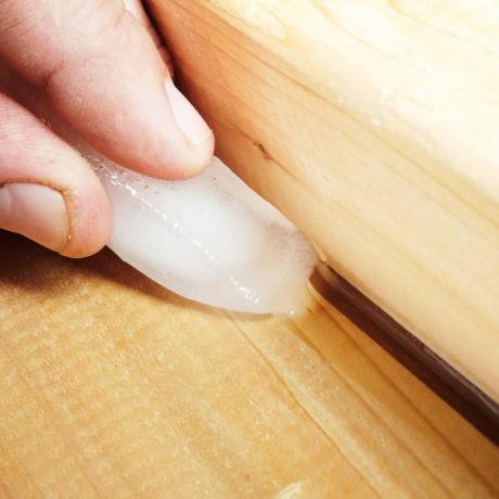 close-up van hand vasthouden en ijsblokje om kit aan te brengen tussen twee stukken hout