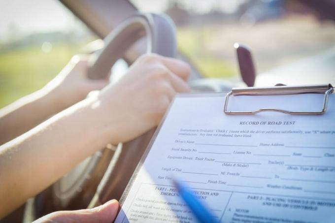 Examinador llenando el formulario de prueba de manejo de licencia de conducir sentado con su estudiante dentro de un automóvil