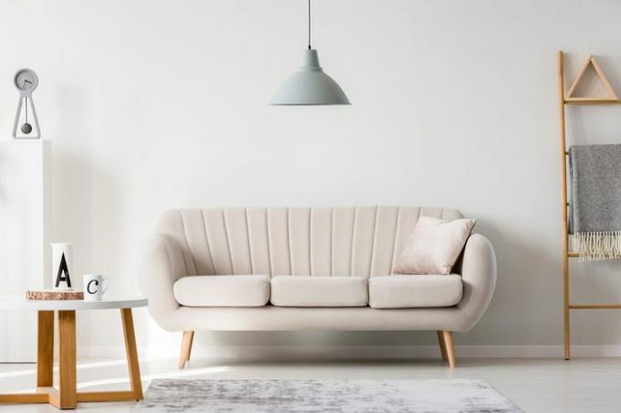 Lámpara gris sobre el sofá beige en el sofisticado salón interior con escalera y mesa redonda de madera