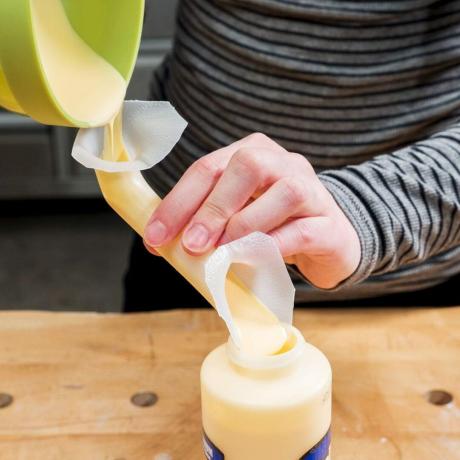 gros plan des mains à l'aide d'un pot à lait comme entonnoir pour verser de la colle dans un petit récipient
