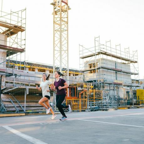 Две жени тичат покрай строителна площадка на открито в града