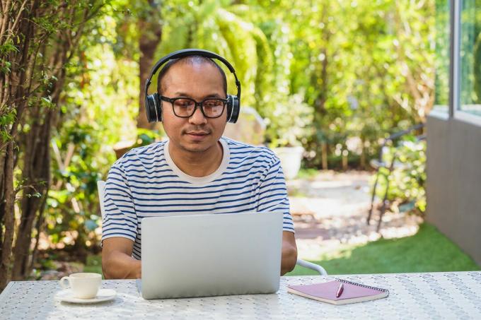 Uomini maturi asiatici che lavorano con un computer portatile e ascoltano musica mentre si trovano nel cortile anteriore o sul retro all'aperto a casa
