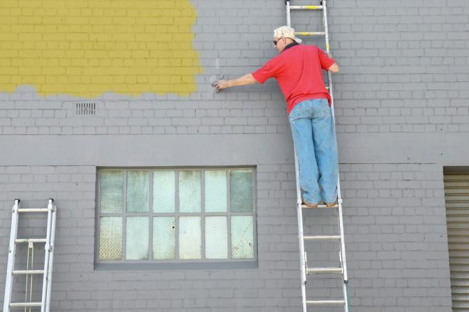 Човек върху стълба рисува екстериор на сграда