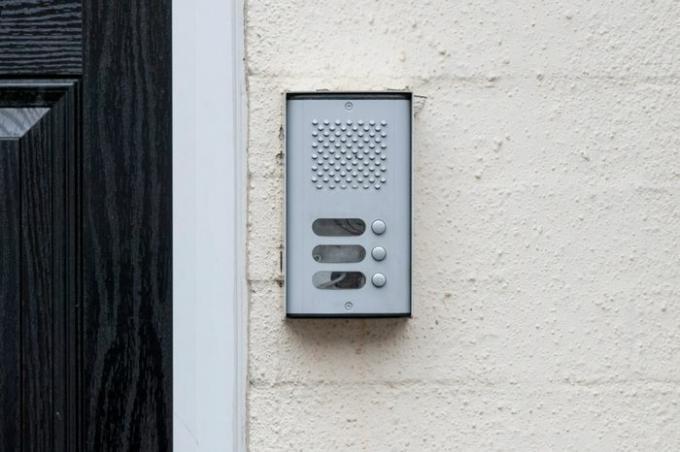 Intercomunicador timbre residencial junto a una puerta negra sobre una pared blanca