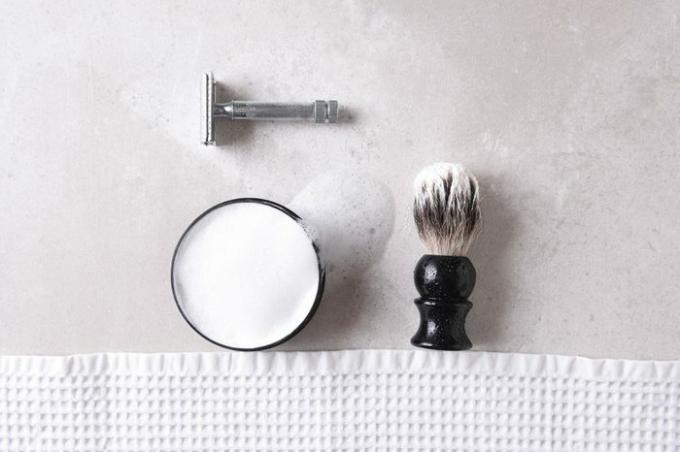 Brivanje tihožitja: Varnostna britvica z brisačo, krtačo in milom na sivi površini ploščice.