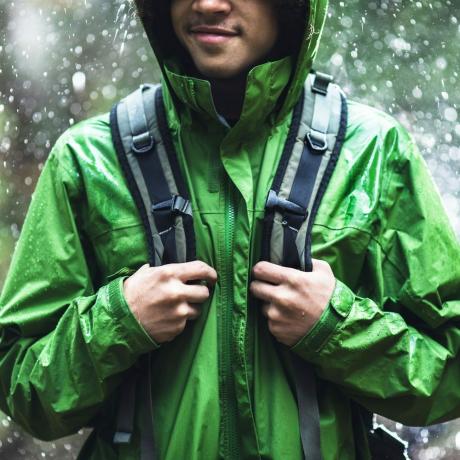 वाटरप्रूफ जैकेट के साथ बारिश में लंबी पैदल यात्रा करता युवक