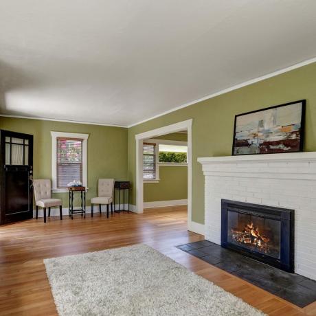 Obývačka-interiérový-dizajn-remeselníka-domova-s bielymi tehlami-krbom-vstavanými-policami-sedadlom-s-vankúšmi-bledo-zelenými-stenami-a-drevenou podlahou