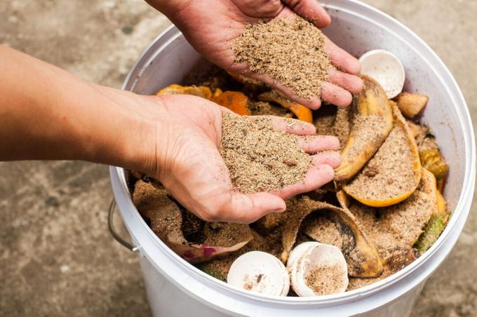 Mladý človek vonku kompostuje kuchynské zvyšky na nádobe z recyklovaného plastu