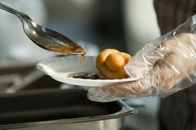 Catering schotel eten, Chinese dumplings met saus. Papieren schaal met knoedel in de ene hand en lepel met saus in de andere hand.