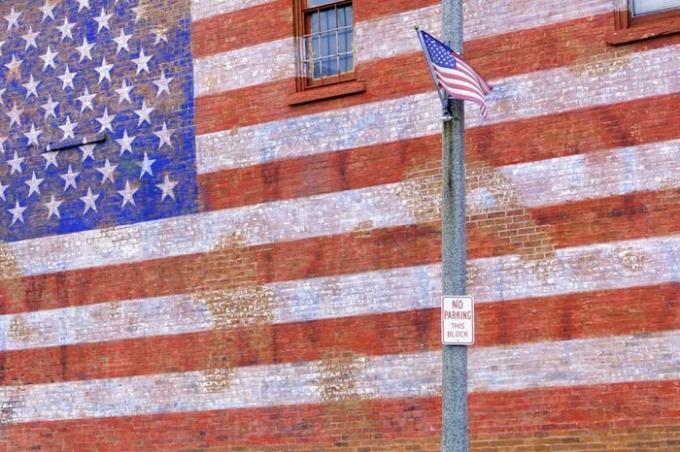 პატარა ქალაქის ქუჩის სცენა ილინოისში: ამერიკის დროშა ნიავიდან აფრიალებს უზარმაზარი მოხატული ამერიკული დროშით, რომელიც ქრება აგურის კედლიდან