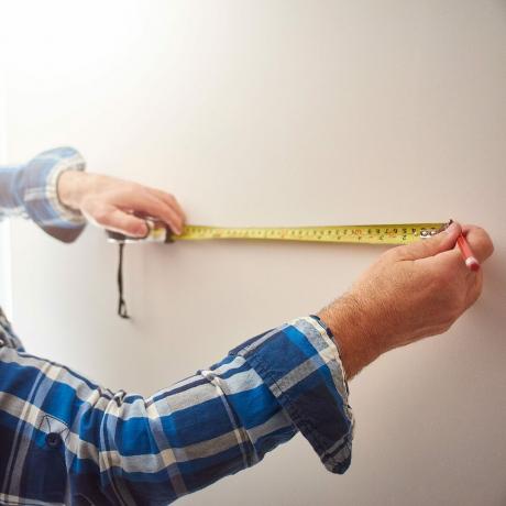El hombre marca puntos en una pared con una cinta métrica