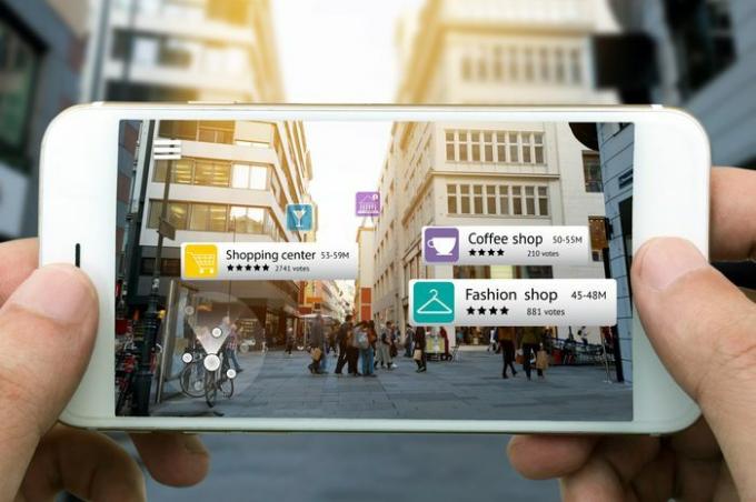 Marketingový koncept rozšírenej reality. Ruka držiaca chytrý telefón pomocou aplikácie AR kontroluje relevantné informácie o priestoroch okolo zákazníka. Mesto a svetlice na svetlom pozadí