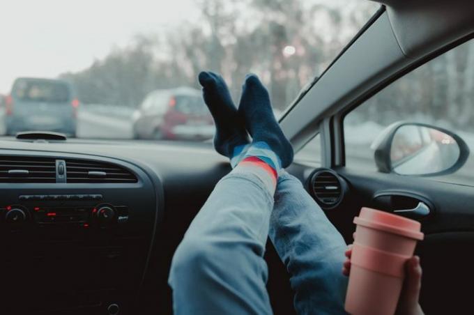 Kobieta trzyma filiżankę kawy wewnątrz samochodu. Styl życia w podróży. Nogi na desce rozdzielczej