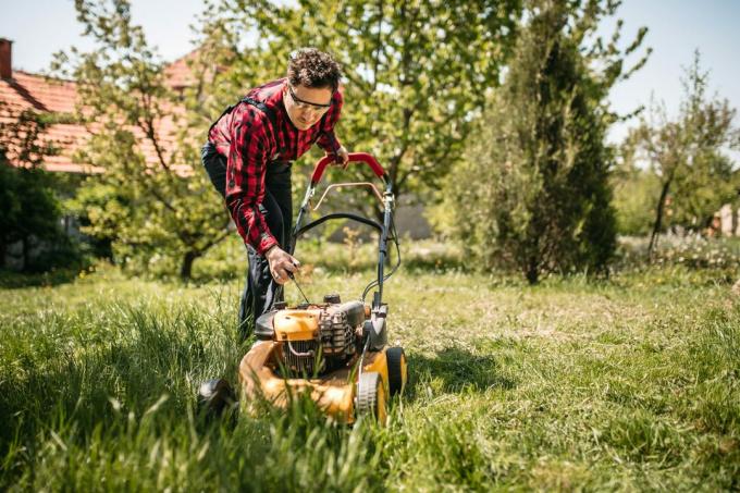 Seorang pria menggunakan mesin pemotong rumput di halaman belakang rumahnya