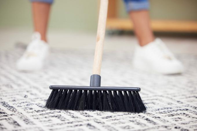 घर में कालीन की सफाई कर रही एक अपरिचित महिला का क्रॉप शॉट