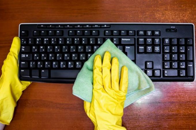 Kobieta w gumowych rękawiczkach dezynfekuje klawiaturę