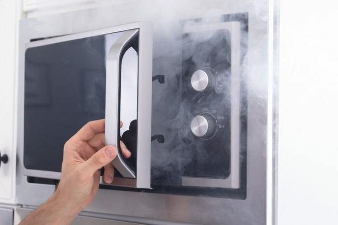 Homem atônito em frente a um forno aceso com fumaça ao redor da cozinha