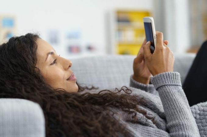 donna sdraiata sul divano mentre scrive un messaggio di testo sul suo cellulare