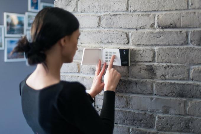 Wanita muda memasukkan pin keamanan pada tombol alarm rumah. Sistem keamanan rumah
