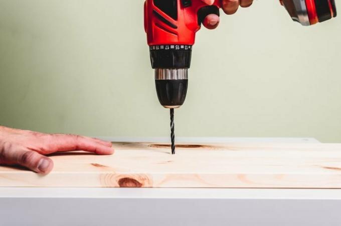 En röd skruvmejsel borrar ett hål i en träskiva. Att göra träprodukter, begreppet manuellt arbete.