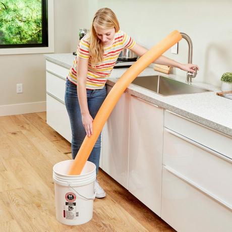 mujer usando un fideo de piscina para llenar un balde en el piso del fregadero de la cocina