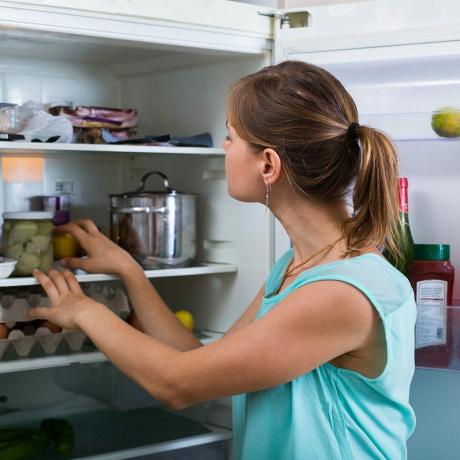 Jonge vrouw staat in de buurt van koelkast gevuld met producten